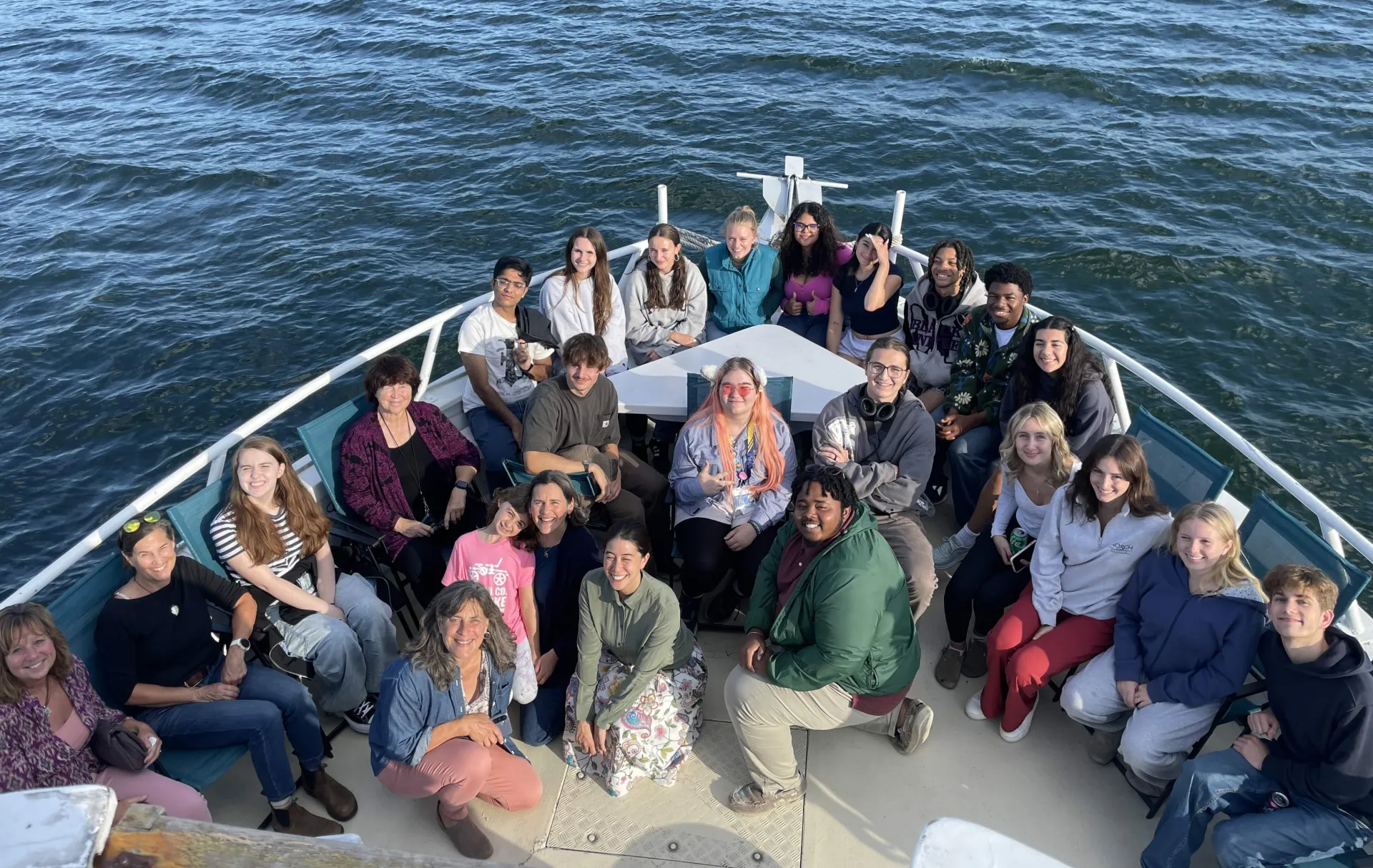 A group of student scholars sitting on the bow of a boat in the sunshine with blue waters in the background 