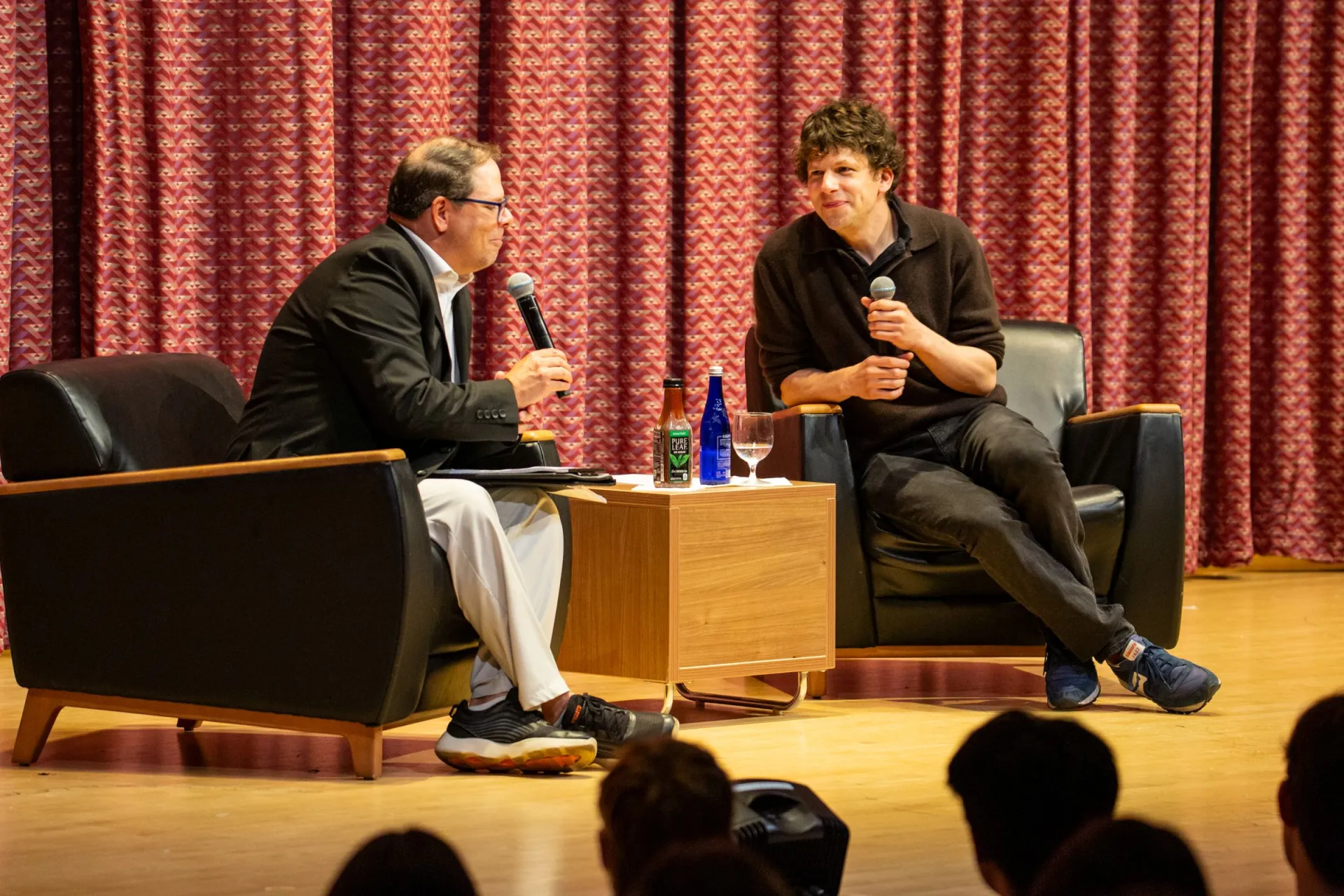 A man interviews actor Jesse Eisenberg on a stage.