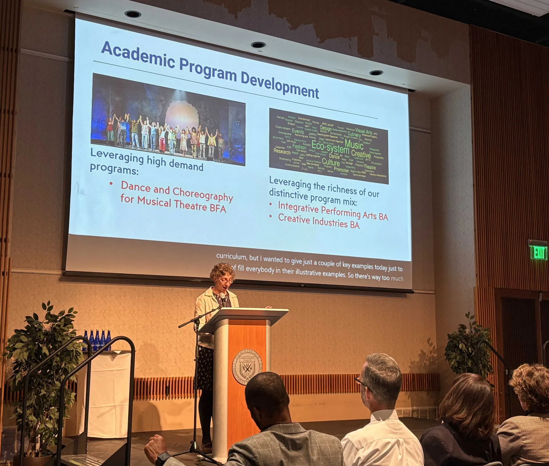 Woman stands at lectern with slide on screen behind her.