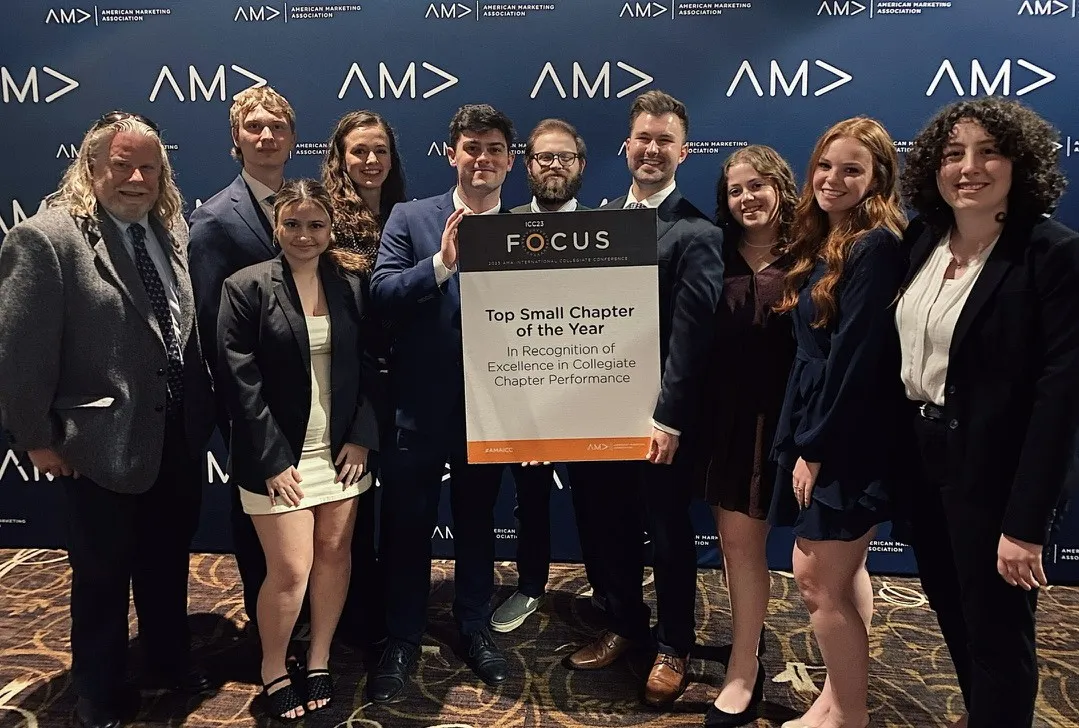 A group of students and their professor with a sign that says "Top Small Chapter of the Year"