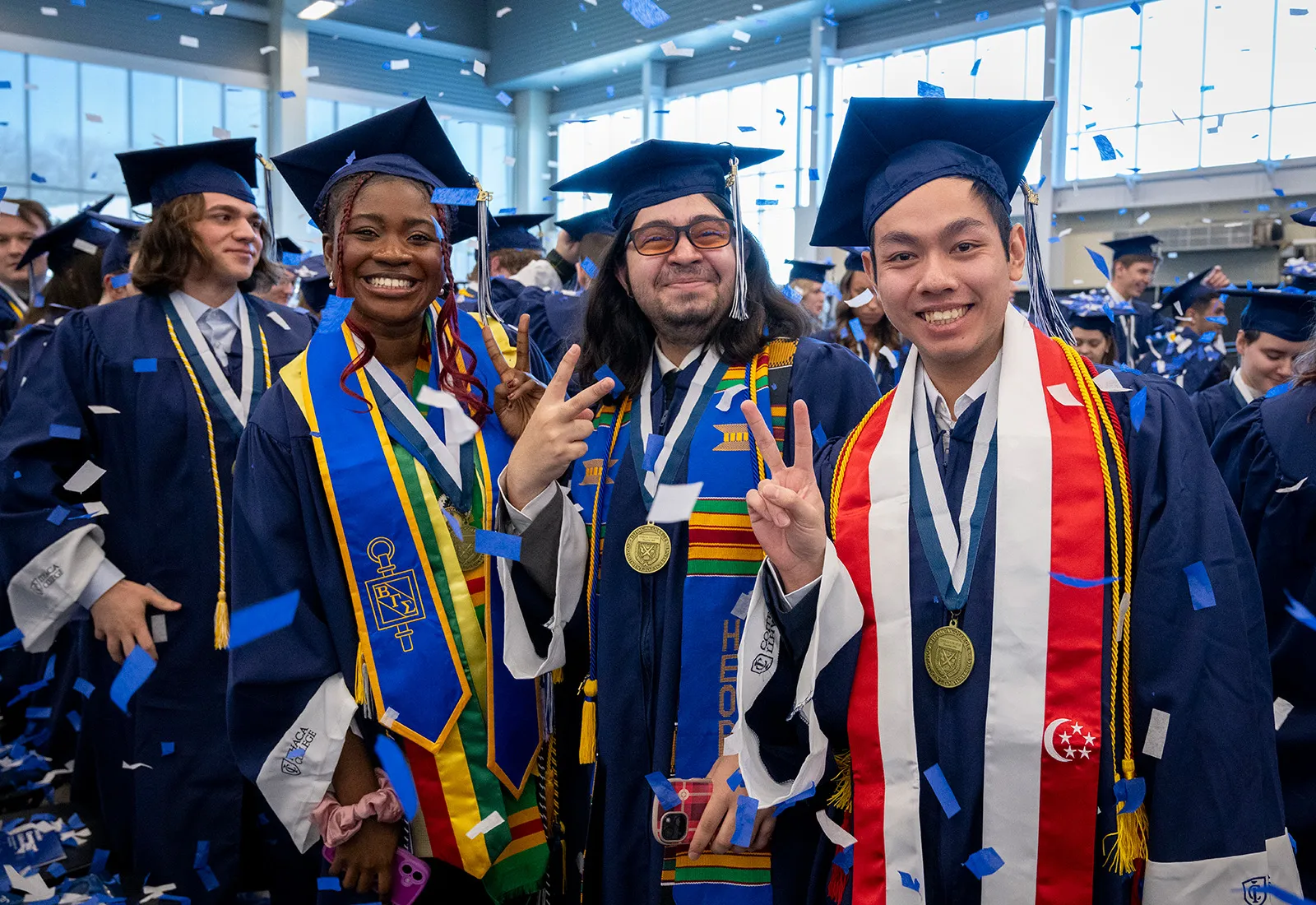 Graduates in caps and gowns pose and smile while confetti falls.