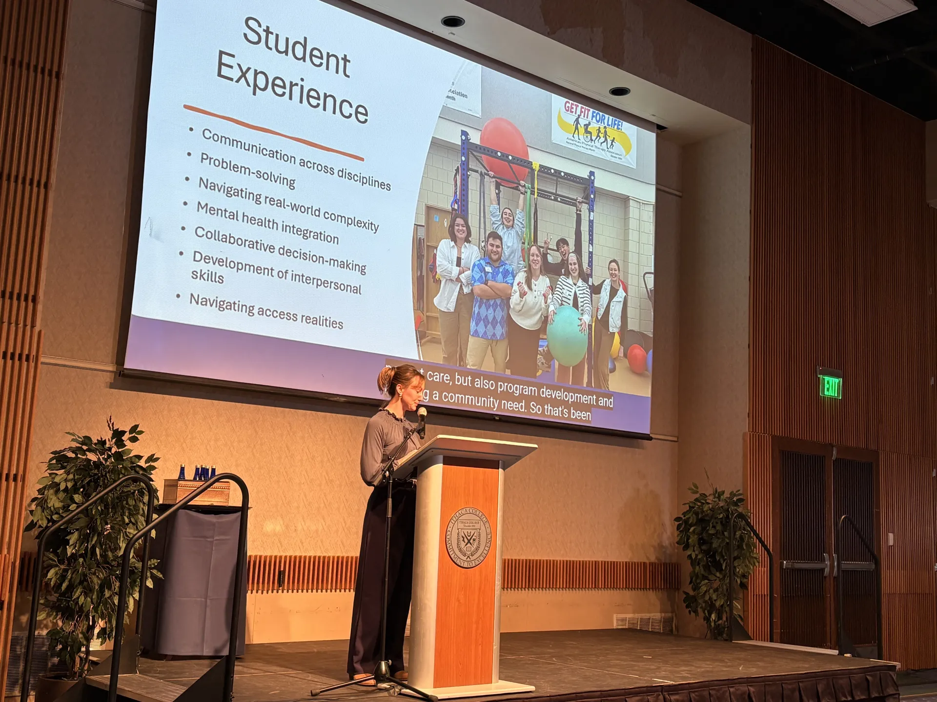 woman standing at a lectern with a slide projected behind her