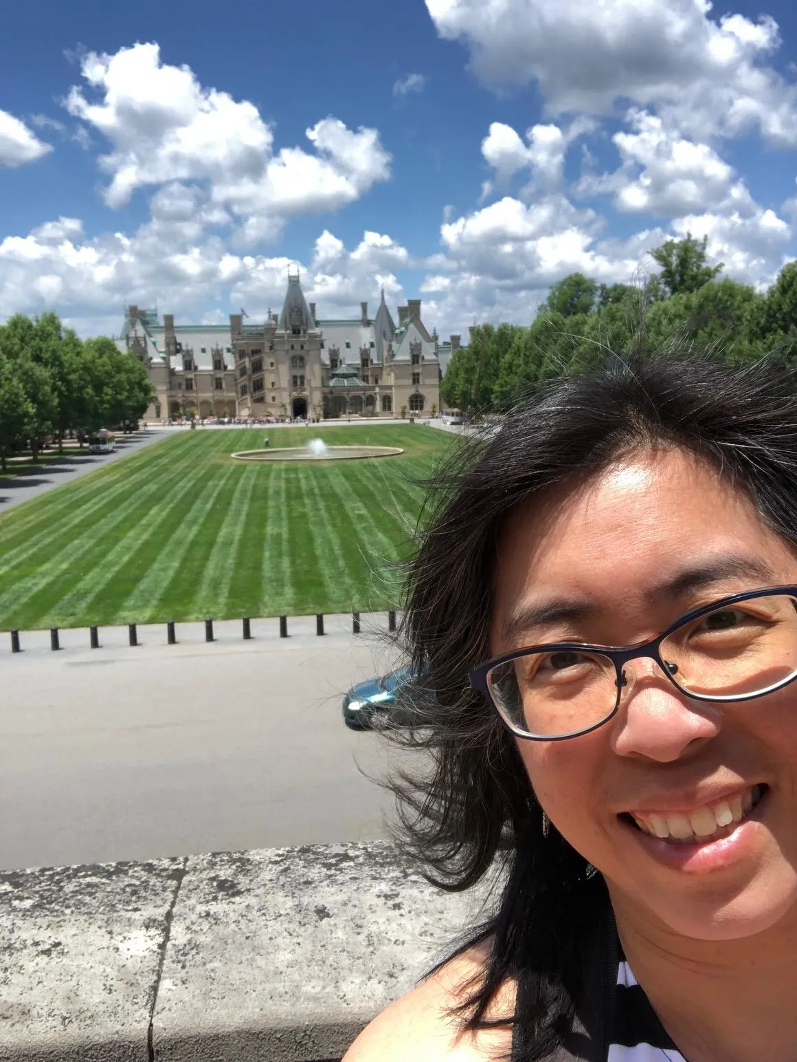 Melody with blue skies and clouds above standing in front of Biltmore estate mansion
