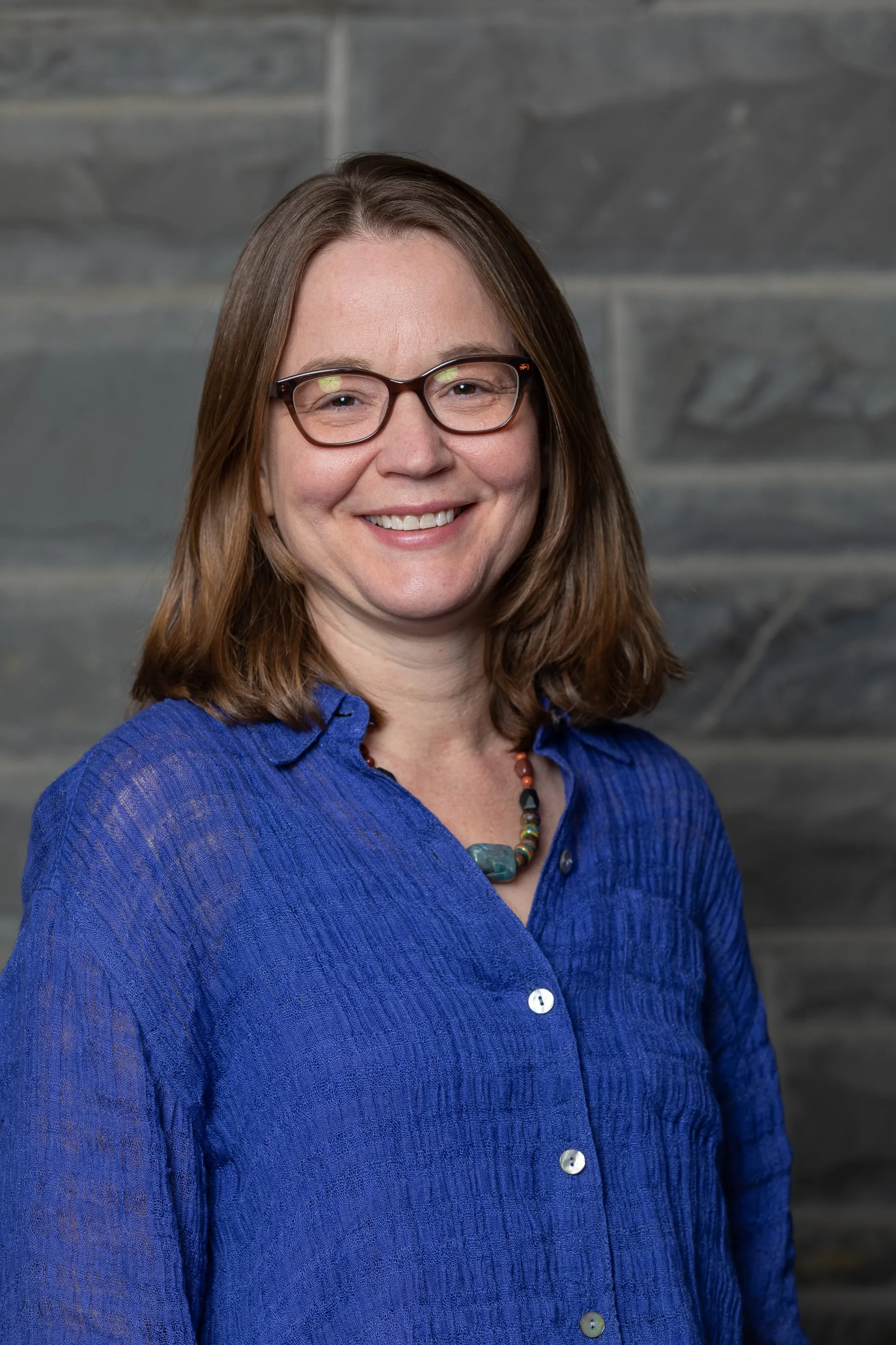 Elizabeth Bergman, Ph.D., Associate Professor at Ithaca College, smiling in front of a stone wall background.