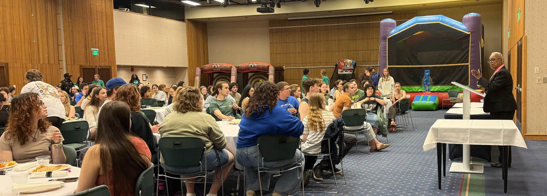 students seated around tables listening to a speaker