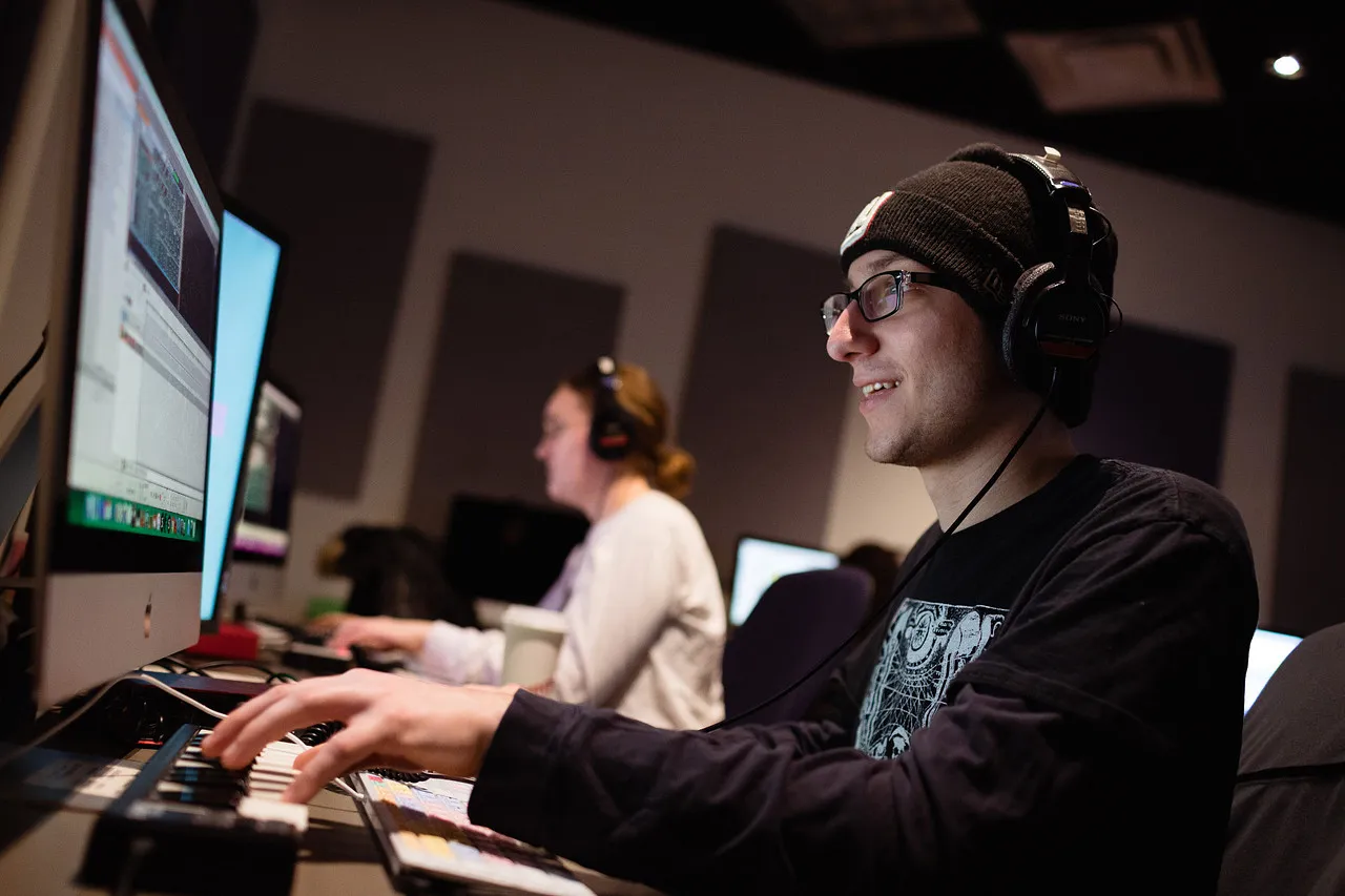 Two students with headphones on looking at computer screens.