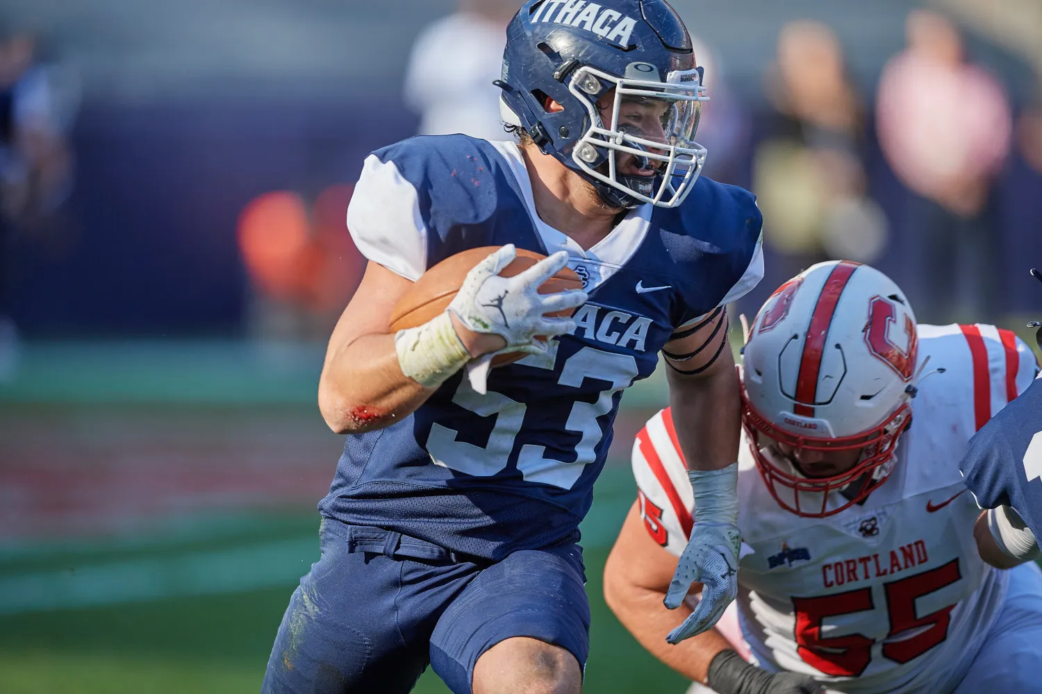 A college football player in a blue uniform evades an opposing player in a red uniform.