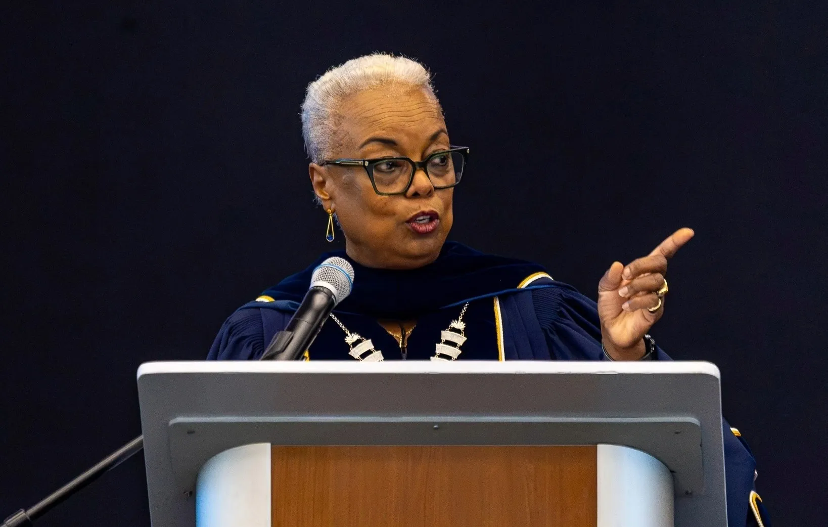 A woman wearing academic regalia speaks at a podium.