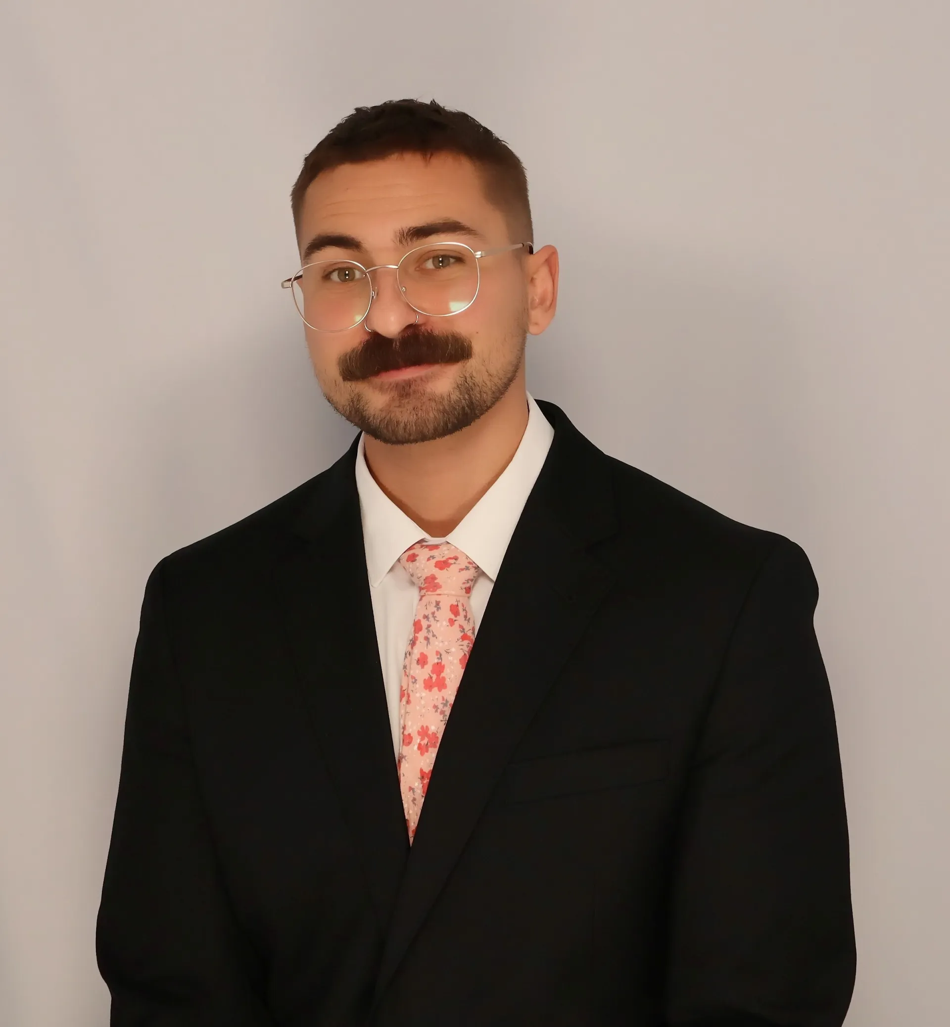 Photo of Julian wearing a black suit and pink tie.