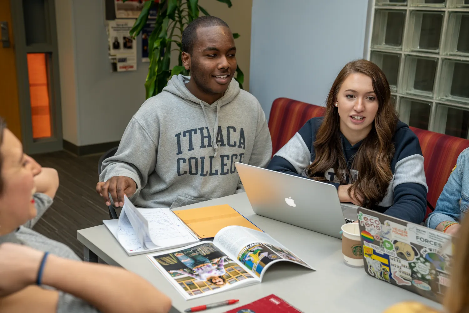 Ithaca College scholars sit at a table with laptops and print media