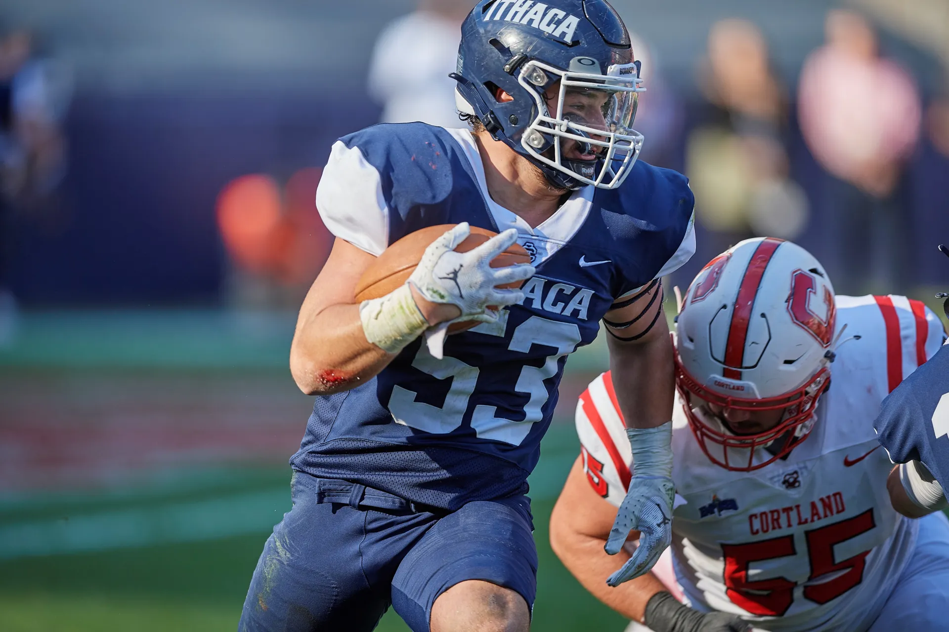 Two college football players, one in a blue uniform and one in a white uniform, compete.