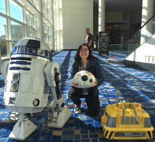 A woman posing with two "Star Wars" droids