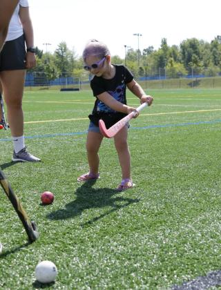 A toddler hits a ball with a field hockey stick