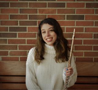 Student holding flute by brick wall