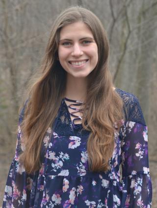 This is a photo of Lauren Bovenzi. Elizabeth is wearing a flowing blue shirt with flowers on it. Elizabeth has long brown hair that is over the shoulders.