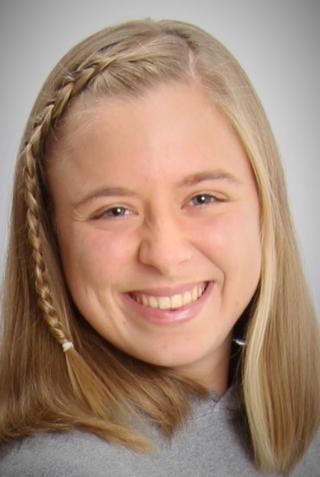 This is a photo of Madelyn McConnon. Madelyn is wearing a gray sweatshirt and smiling broadly for the camera. There is a side braid in the hair.