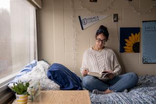 student sitting on her bed and studying in her dorm room