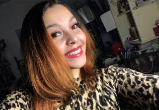 A young woman in an animal print shirt with brownish red hair takes a selfie, smiling