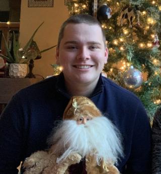Person smiling in front of tree holding a bearded doll