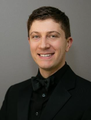 Person in black shirt and bow tie smiling in front of grey wall