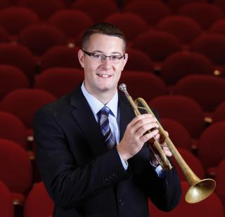 Picture of a man in a suit holding a trumpet in an auditorium