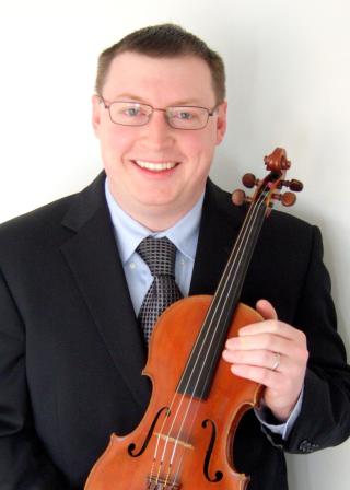 Person wearing suit and tie smiling while holding violin