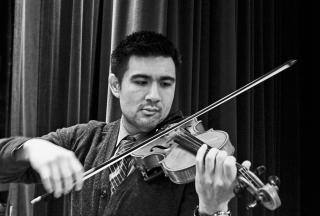 Black and white photograph of person playing the viola in front of curtain