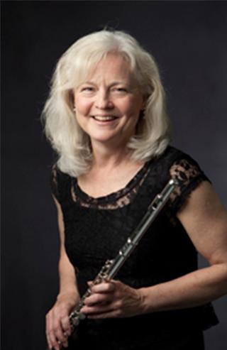 Person smiling while holding flute in front of dark background