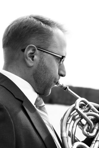 Black and white portrait of person in suit playing French Horn