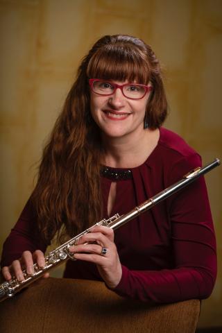 Person wearing glasses smiling while holding flute in front of backdrop