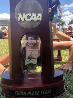 Senior captain, Alli Arndt, gets down to get a view through the team 3rd place NCAA trophy.