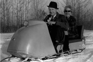 Older couple on an old-fashioned snow mobile.