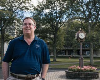 Dave Prunty standing in front of the clock on the academic quad