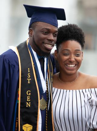 A male student in graduation regalia standing next to a woman