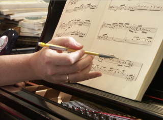 A person's hand is holding a pencil hovering over musical notation.