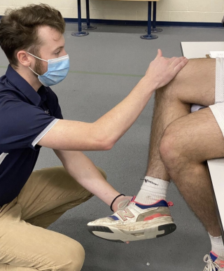 Photo of a physical therapy student assessing the knee of a student athlete