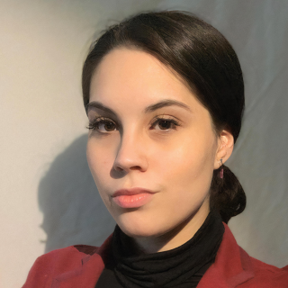 Cassandra is looking at the camera with her body slightly turned away in front of a white background. She is wearing a red blazer with a black turtleneck and her hair is pulled back into a low bun.