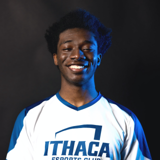 Mark is standing in front of a black background smiling at the camera. He is wearing an Ithaca College esports club jersey in blue and white.