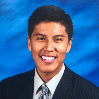Cesar is smiling at the camera in a blue pin stripped suit with a blue background behind him.