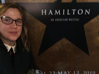 Angela Branneman, Associate Professor of Theatre Arts Management in front of Hamilton poster.