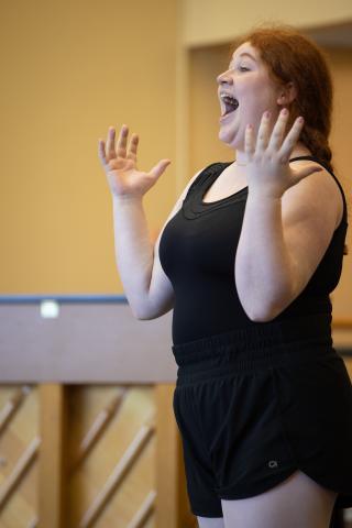 A student in a black leotard is singing expressively.