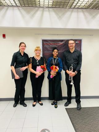 Four people smiling and standing together after a performance at the American International School in Dhaka.