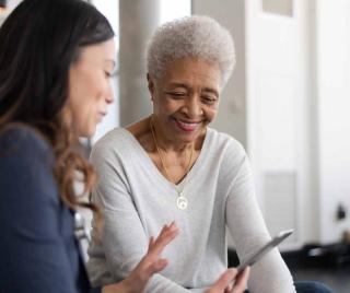 Older adult woman learning about a smart device from a younger woman