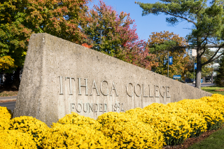 The Ithaca College sign at the entrance to the College - brass letters on a triangular cement block - surrounded by yellow geraniums