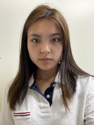 Mia is posing for photo on white background. Is wearing a white polo shirt with red and blue accents. Has long dark hair extending past shoulders. Is not smiling.