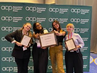 Four students hold up Pacemaker Award plaques in front of a green step and repeat backdrop.