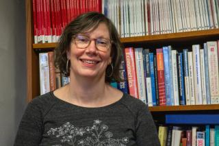 Photo shows Professor Shaianne Osterreich in front of her office bookshelf. 