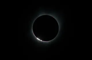 Solar eclipse near totality: a dark circle surrounded by a white halo.