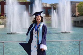 Sammi standing in front of the Ithaca College fountains in her Ithaca College undergraduate commencement cap and gown. 