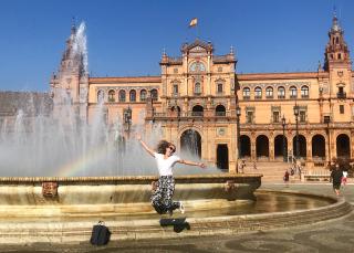 A woman jumping in the air in front of a fountain in Plaza de Espana, Seville, Spain